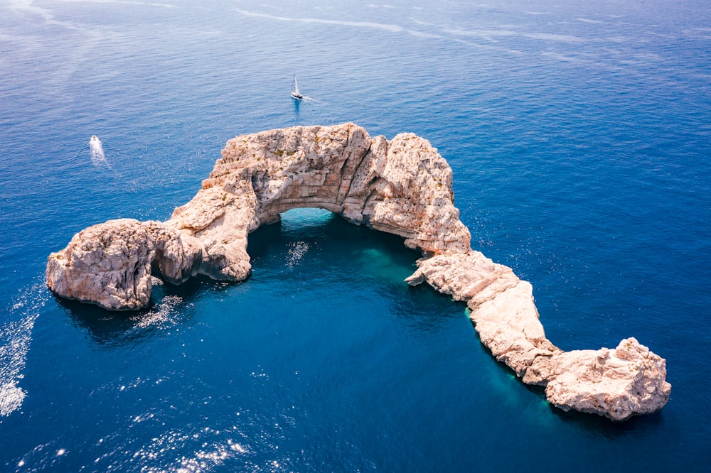 personne debout sur une formation rocheuse au milieu de la mer pendant la journée