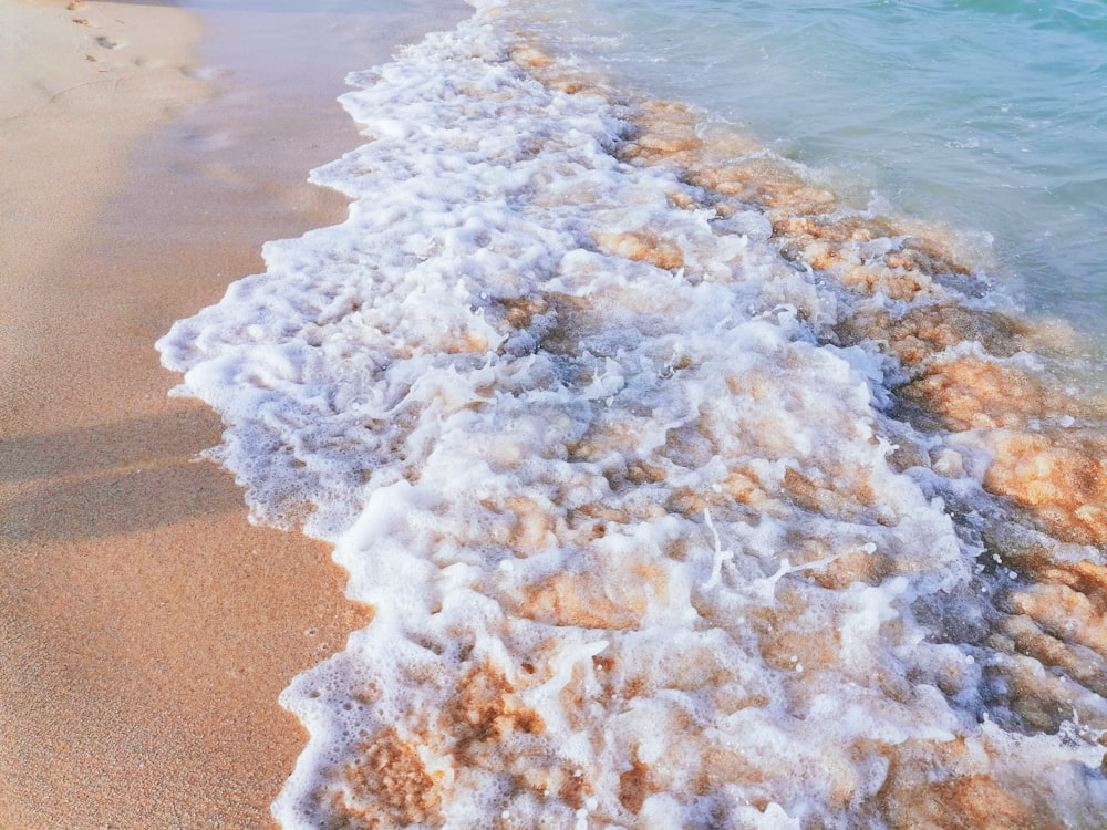 日中の茶色の砂浜に白と茶色の海の波