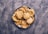 A metal plate holds a stack of golden-brown fried flatbreads arranged neatly in a circular fashion. The background is a textured grey surface, providing contrast to the warm tones of the bread.