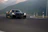 A close-up of a sleek mach1 performance car speeding along a winding mountain road at sunset.