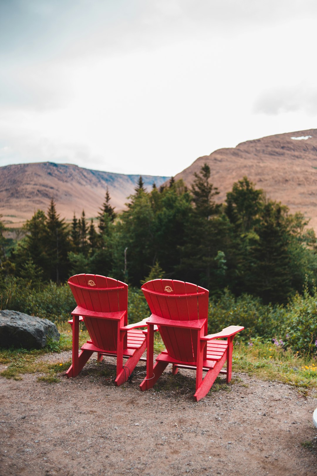 two red wooden armchairs on gray rock near green trees during daytime