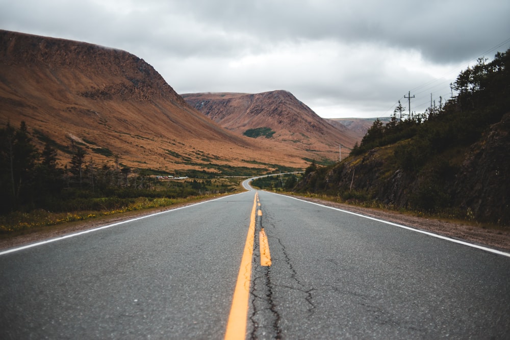 gray concrete road near brown mountain under white sky during daytime