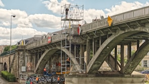 people riding on blue and black motorcycle under gray bridge during daytime