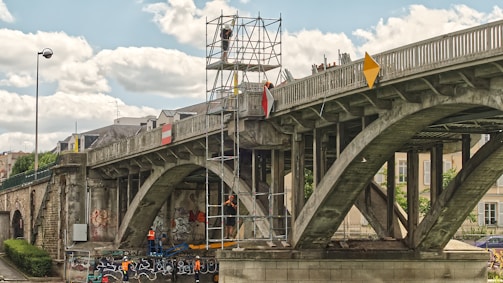 people riding on blue and black motorcycle under gray bridge during daytime