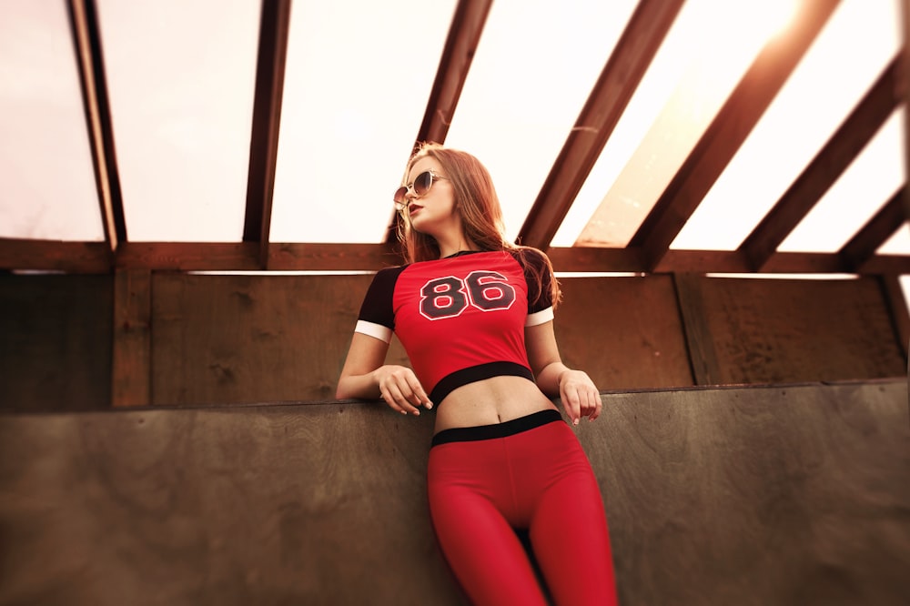 Frau in rot-schwarzem Tanktop und rosa Leggings sitzt auf brauner Holztreppe