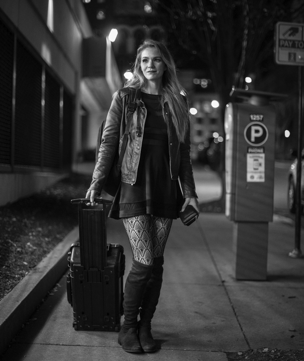 grayscale photo of woman in jacket and pants standing on sidewalk