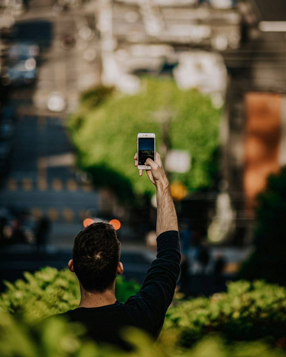 man in black long sleeve shirt holding black smartphone taking photo of city buildings during daytime