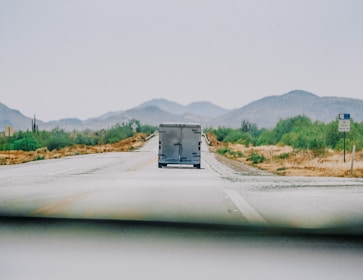 A truck driving on a highway surrounded by green fields.