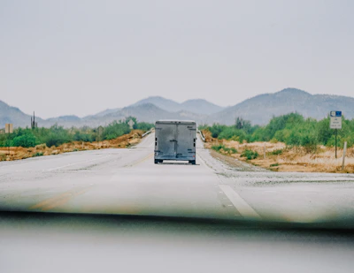A vibrant photo of a moving truck navigating a desert highway under a clear blue sky.