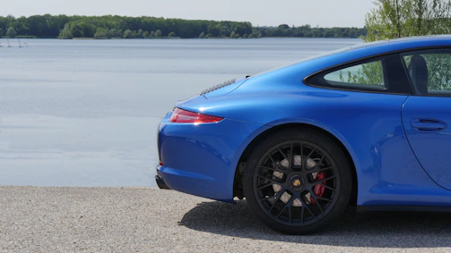 A sleek, shiny car parked by a coastal driveway with soft aqua blue skies overhead.