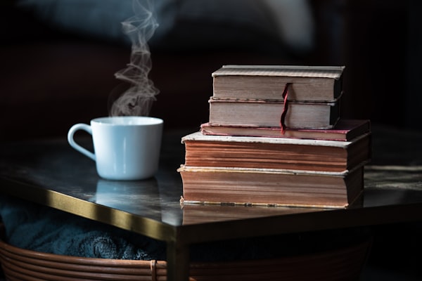 A steaming cup of coffee on a desk next to a stack of old books.