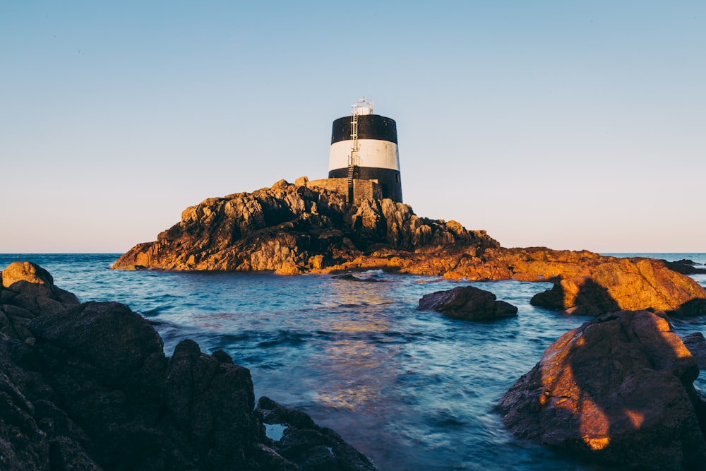 white and black lighthouse on brown rock formation near body of water during daytime