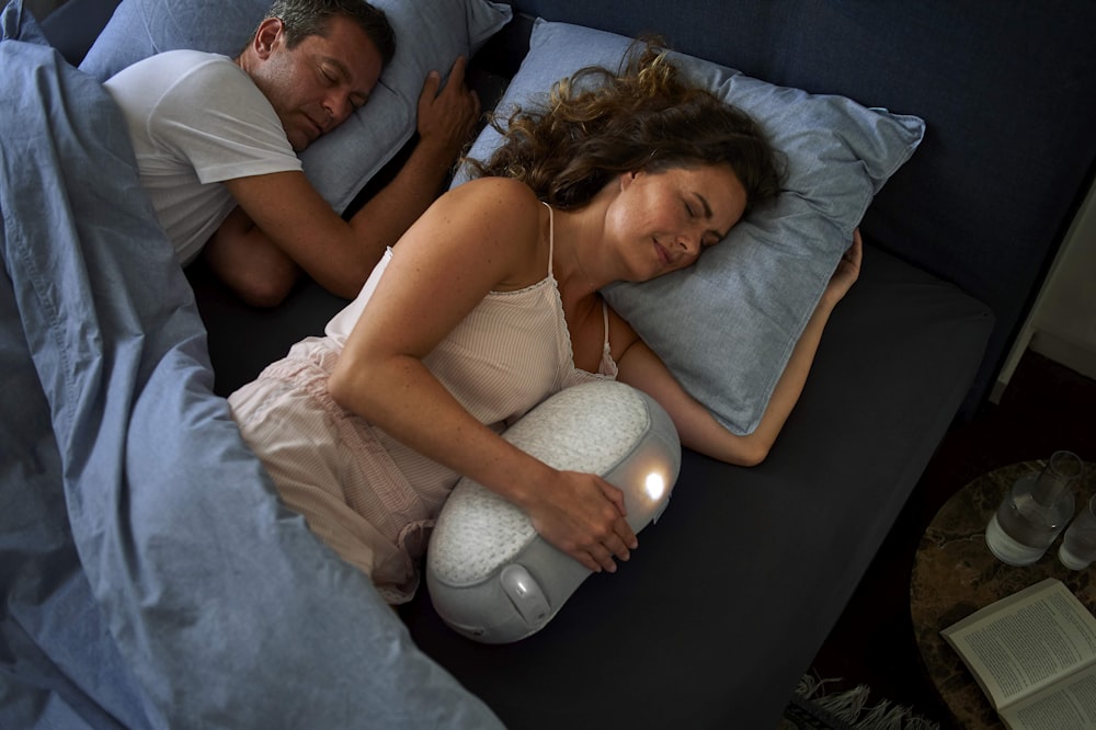 woman in white tank top lying on bed beside man in black shirt