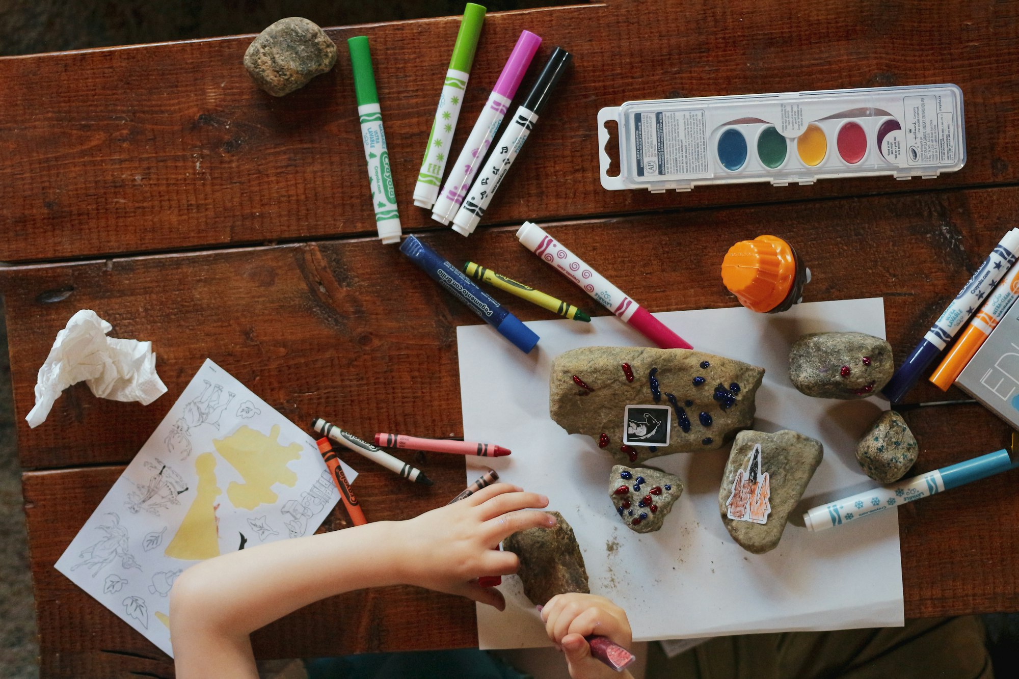 A child drawing on rocks and paper.