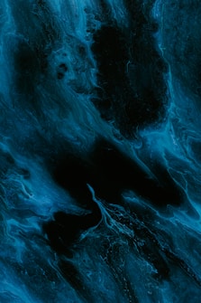 A swirling abstract pattern with a mixture of deep blues and blacks, creating a fluid and dynamic appearance reminiscent of ink in water or cosmic phenomena.