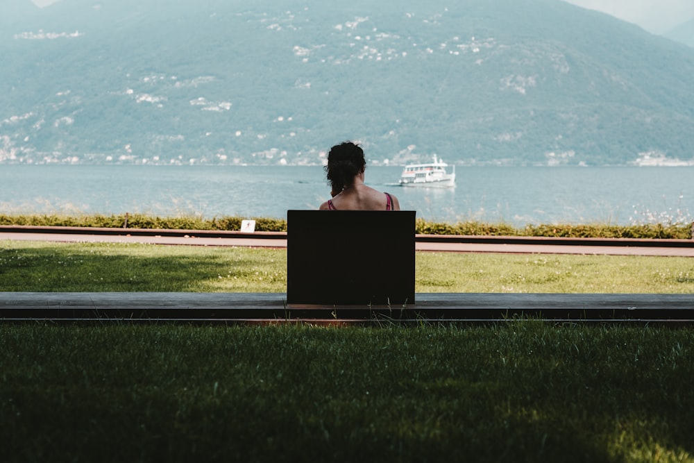 woman sitting on bench looking at the sea during daytime