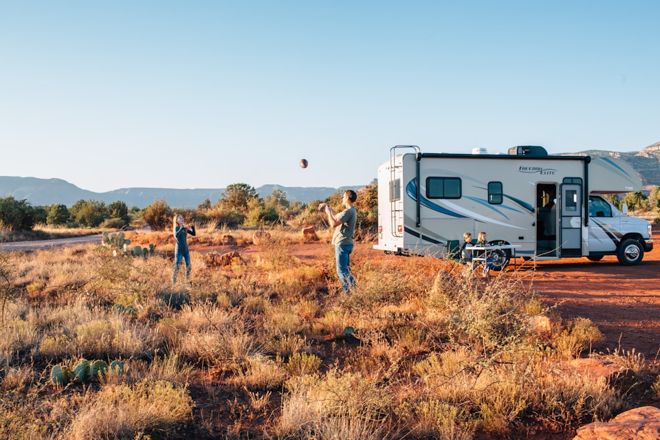 Class-C motorhome parked in desert, two people tossing football.