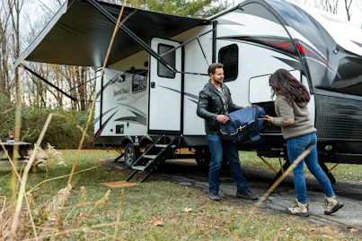 A woman happily setting up her RV campsite surrounded by nature.