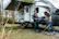 A happy family unloading camping gear from a rumbolibre trailer in a sunny forest clearing.