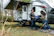 A couple enjoying a scenic view next to their new trailer in a lush campsite.