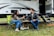 A couple smiling next to a mobile home on their newly acquired land.