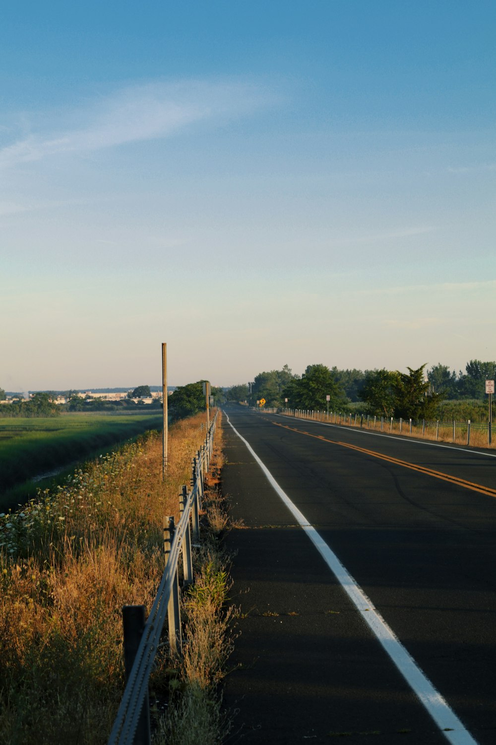 gray concrete road between green grass field under white sky during daytime