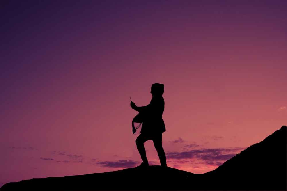 silhouette of man jumping on rock during sunset