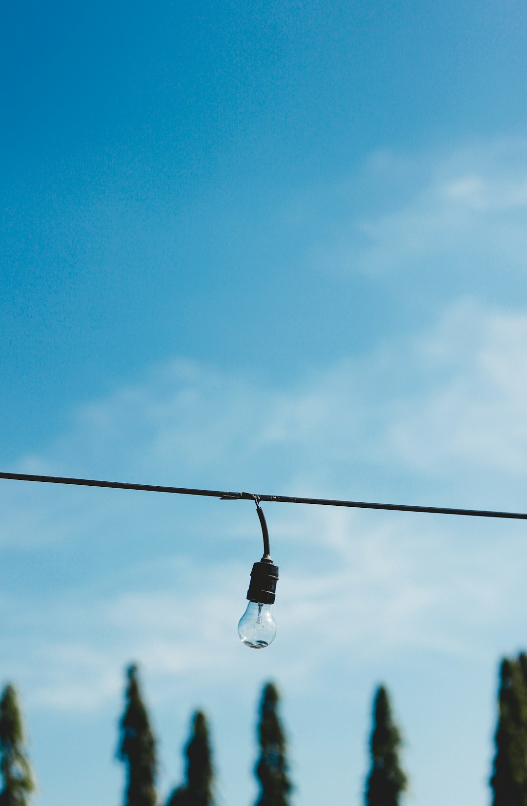 white light bulb on black electric wire under blue sky during daytime