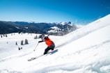 person in orange jacket and black pants riding ski blades on snow covered mountain during daytime