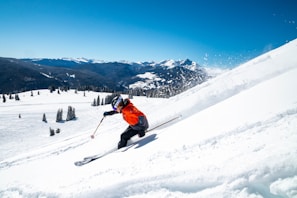 person in orange jacket and black pants riding ski blades on snow covered mountain during daytime