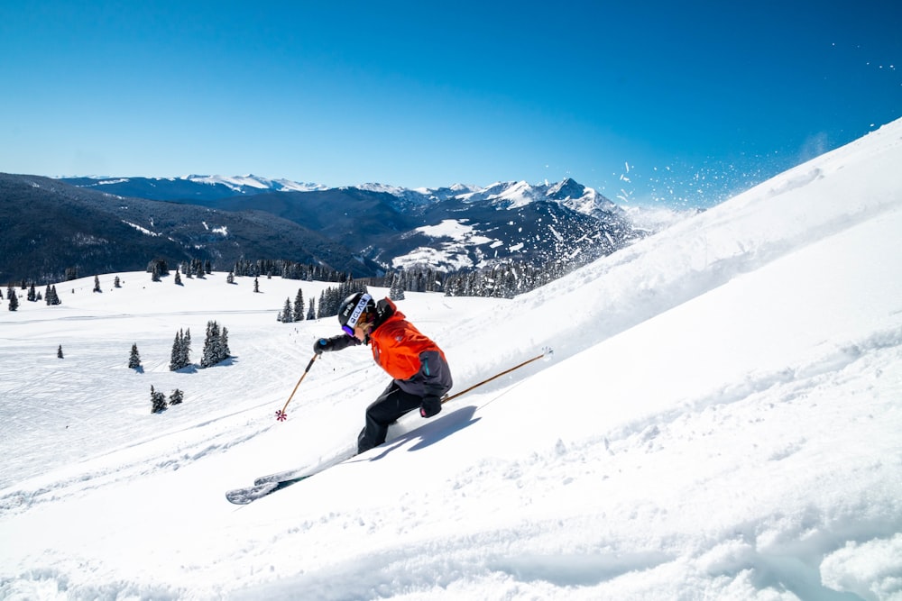 オレンジ色のジャケットと黒いズボンを着た人が、昼間、雪に覆われた山でスキーブレードに乗っている