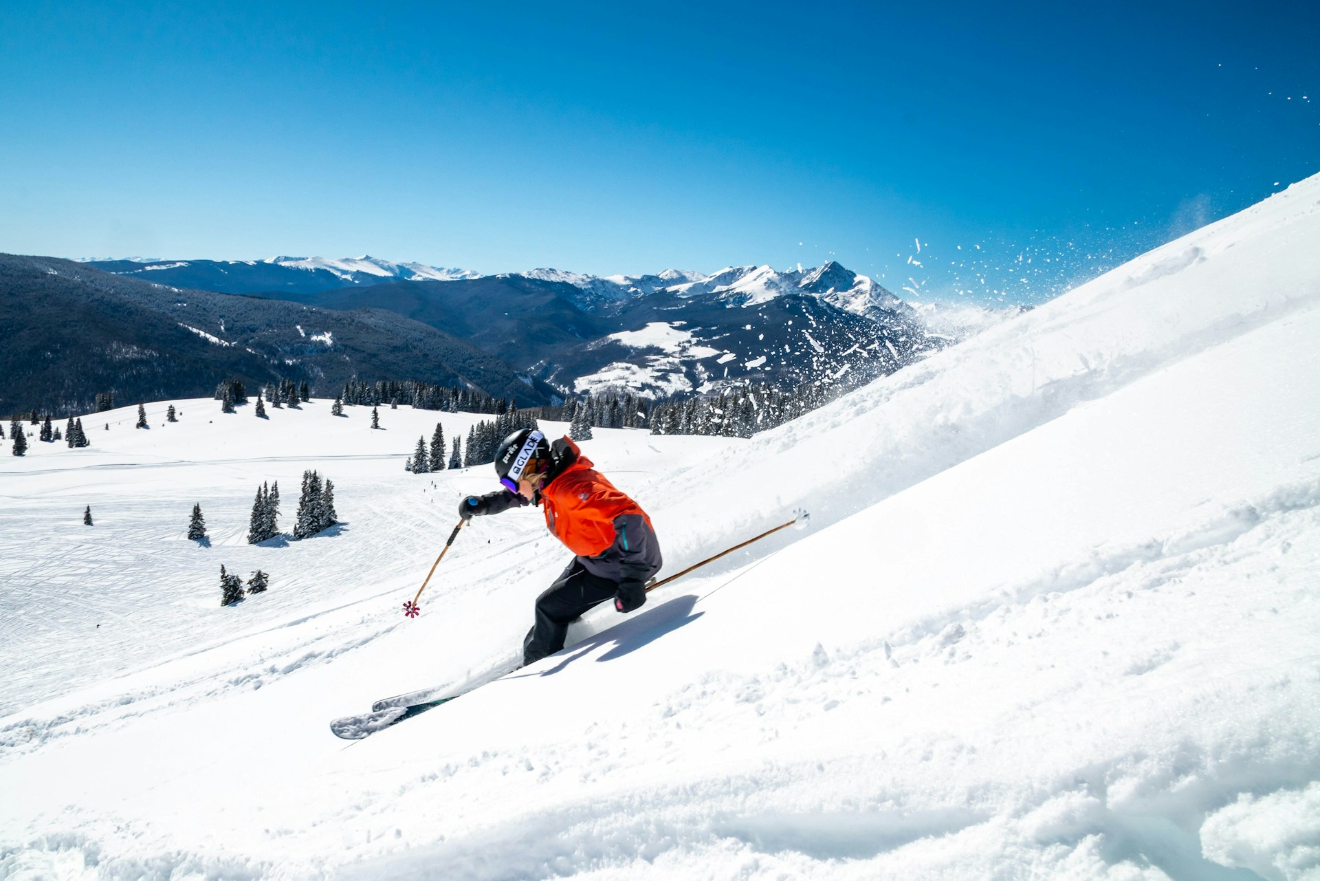 Person in orange jacket riding ski blades on snow covered mountain