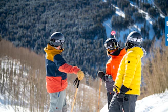 2 men in red and yellow jacket and helmet riding ski blades on snow covered mountain