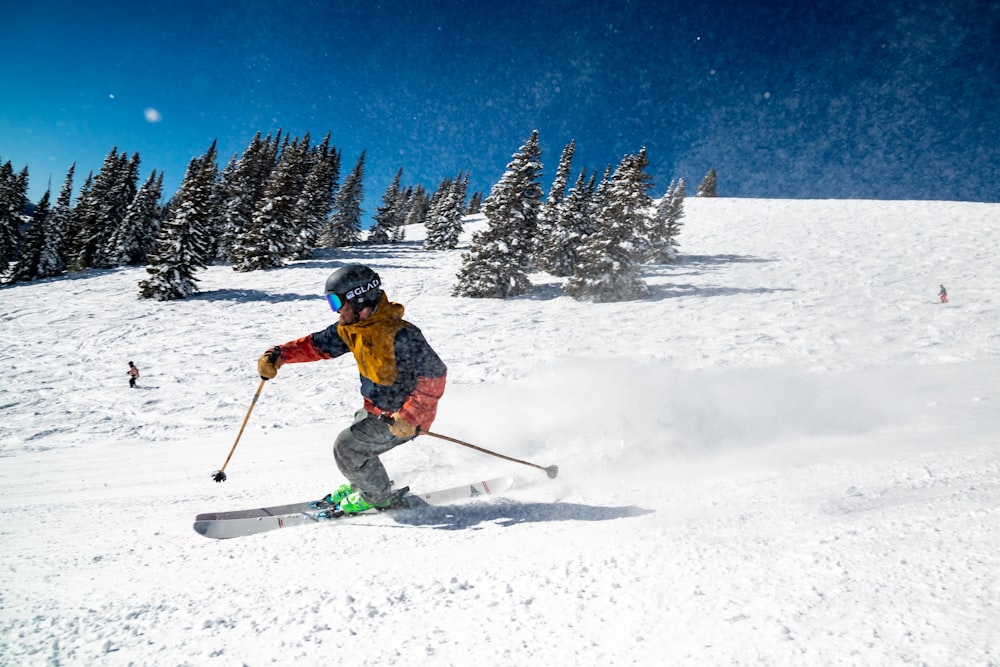 pessoa em jaqueta vermelha e calças azuis cavalgando em lâminas de esqui no chão coberto de neve durante