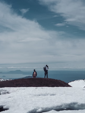 Hikers standing atop a mountain ridge, gazing at a vast valley below.