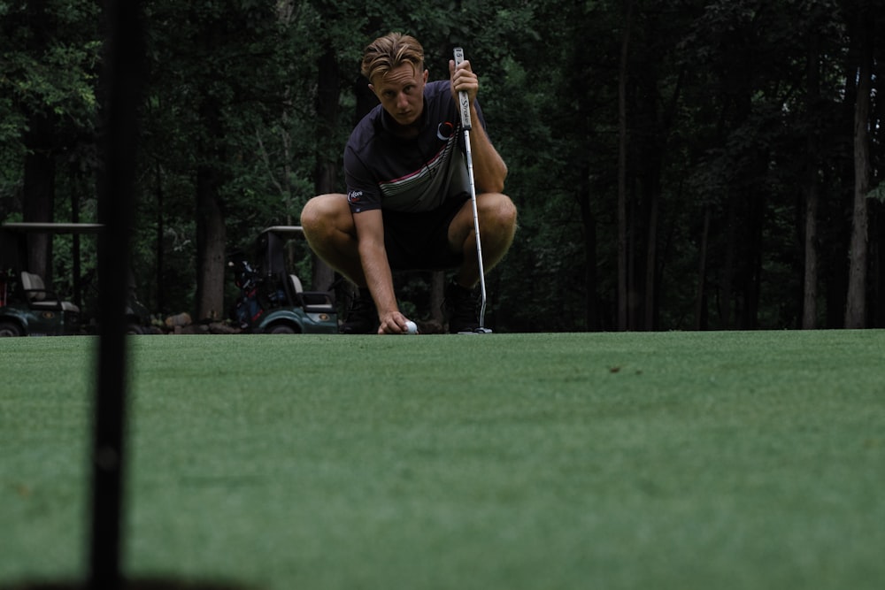 man in black t-shirt and black shorts sitting on golf club during daytime