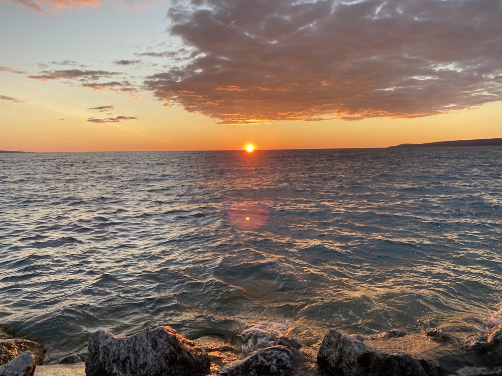 the sun is setting over the ocean with rocks in the foreground