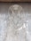 Intricate wire art depicting a human figure with delicate, swirling patterns. The figure has an ornate headpiece and a halo-like ring around its head, set against a textured gray background.