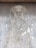 Intricate wire art depicting a human figure with delicate, swirling patterns. The figure has an ornate headpiece and a halo-like ring around its head, set against a textured gray background.