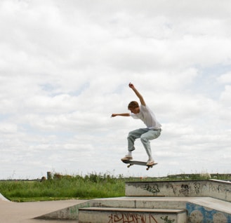 man in white shirt and blue denim jeans jumping on brown concrete bench during daytime