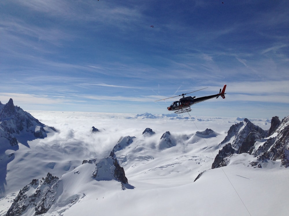 red and black helicopter flying over snow covered mountain during daytime