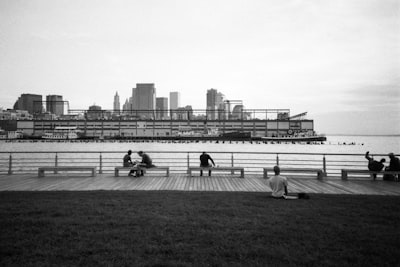 grayscale photo of people sitting on grass field near body of water sparse zoom background