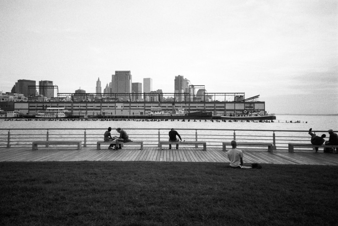 grayscale photo of people sitting on grass field near body of water