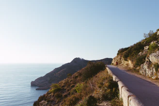 A candid photo of Radit cycling along a coastal road with the ocean and mountains in the background.