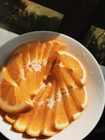 Sunlight streaming over a vibrant orange stoneware plate filled with fresh fruit.