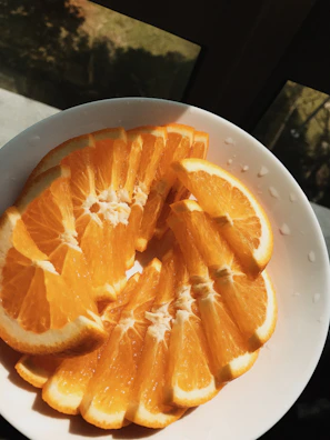 Sunlight streaming over a vibrant orange stoneware plate filled with fresh fruit.