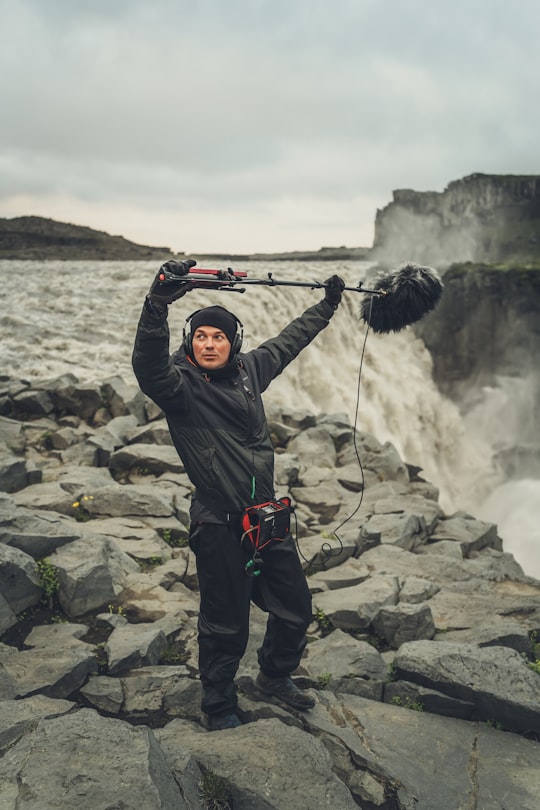 man in black jacket and black pants holding black and gray fishing rod in Dettifoss Iceland