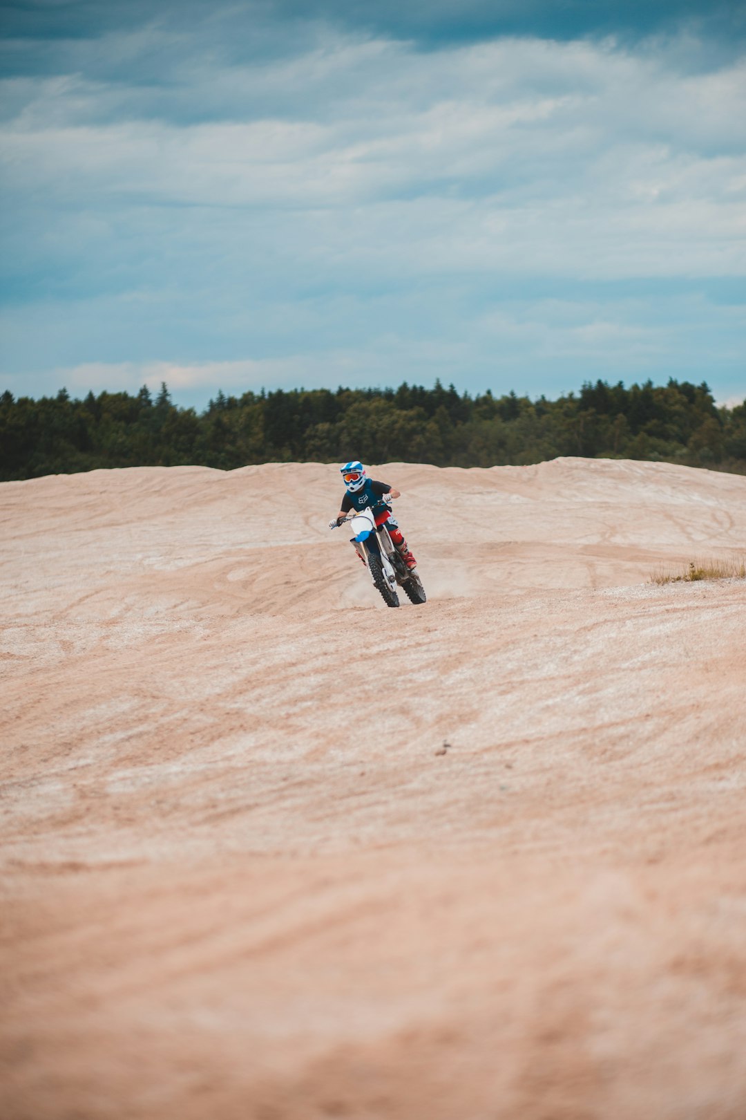 man in blue and red jacket riding motocross dirt bike on brown field during daytime