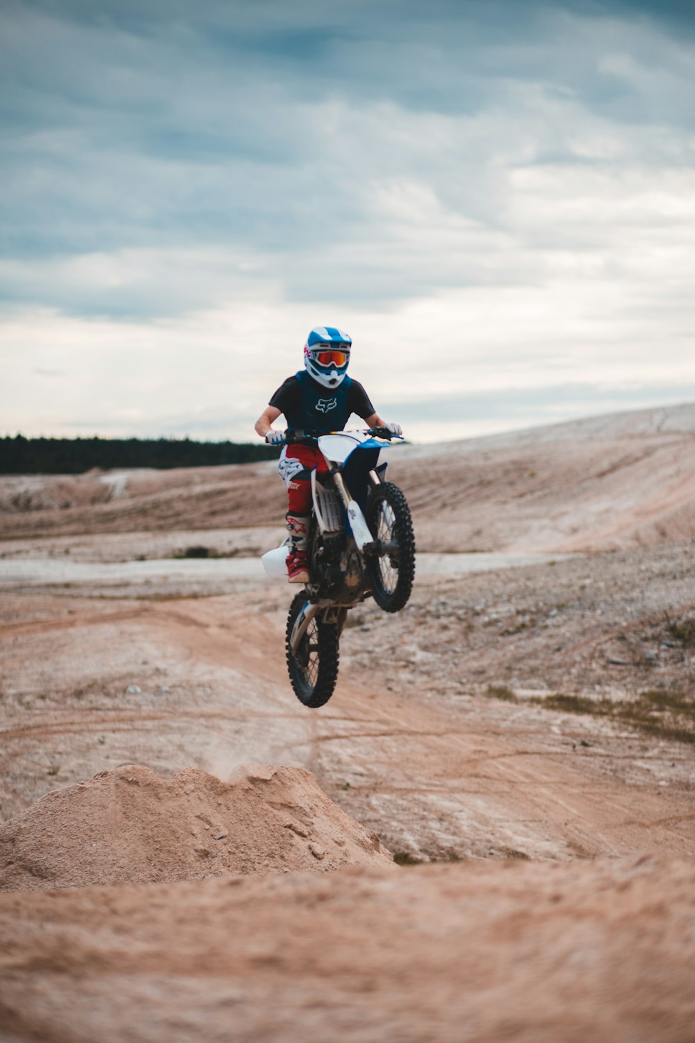 man in red and black motocross suit riding motocross dirt bike on brown dirt road during