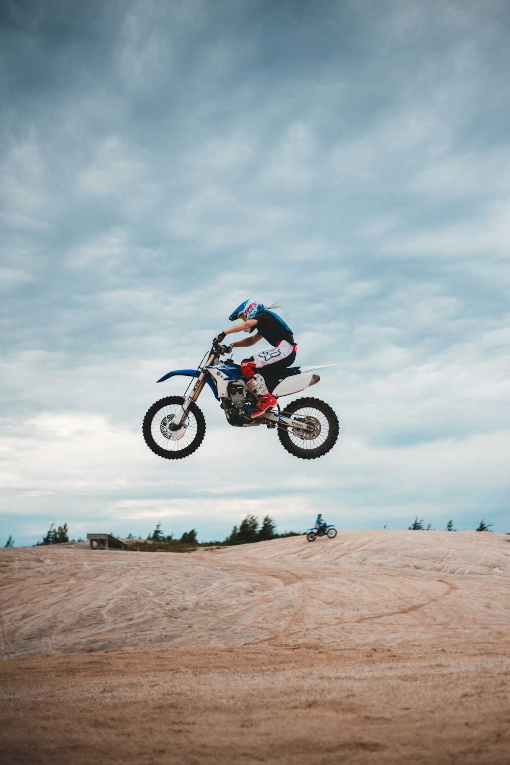 homme conduisant une moto tout-terrain de motocross sur du sable brun sous des nuages blancs pendant la journée